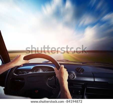 Driver\'s hands on a steering wheel and motion blurred road and sky