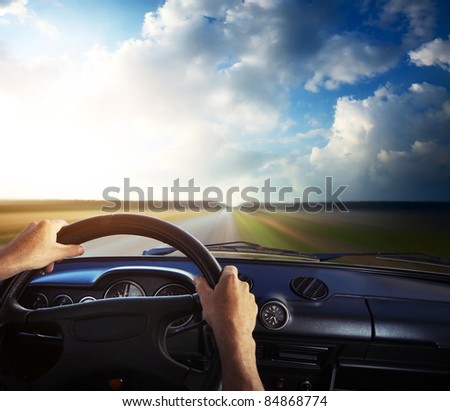 Driver\'s hands on a steering wheel and motion blurred road