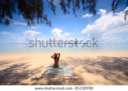 Young woman sitting in tree\'s shadow in swimsuit