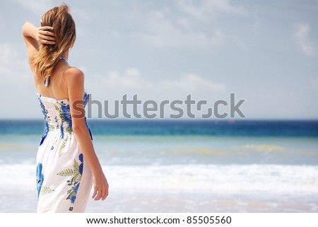Young woman in summer dress standing on a beach and looking to the horizon