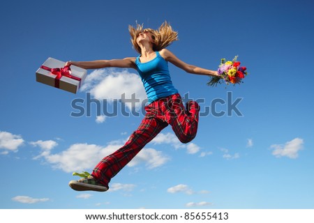 Young woman jumping with a gift box and bouquet of flowers