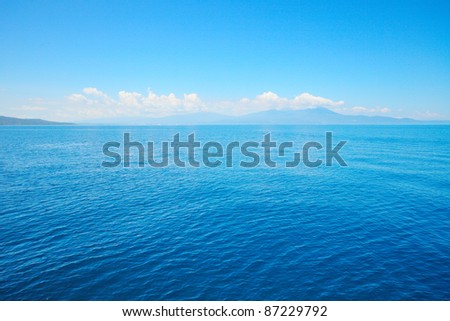 Tropical blue sea and blue sky with sun. Mountains on the horizon