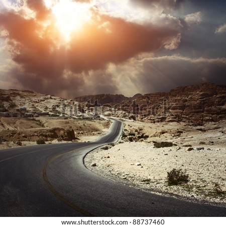 Asphalt road in a desert with dark cloudy sky on the background