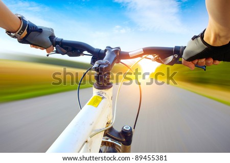 Hands in gloves holding handlebar of a bicycle. Motion blurred asphalt road