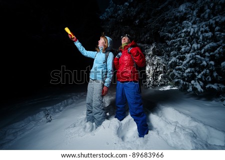 Women with backpacks exploring deep wild forest at night with a torch