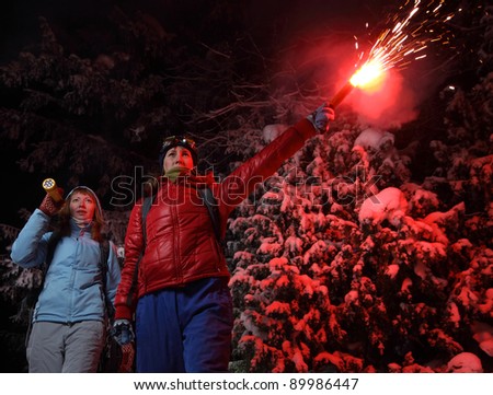 Women with backpacks exploring deep wild forest at night with a torch and red flare