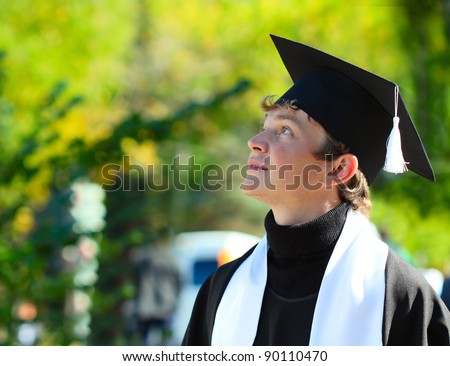 Young student in a hat and gown looking to somewhere against green background
