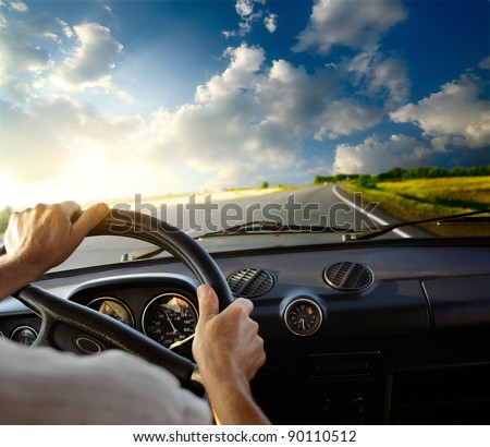 Hands of a driver on steering wheel of a car and empty asphalt road