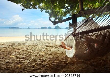 Woman lying in a hammock in tree\'s shadow on a beach