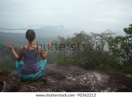 Young woman relaxing on top of a mountain with view to valley. Rainy weather, wet clothes.