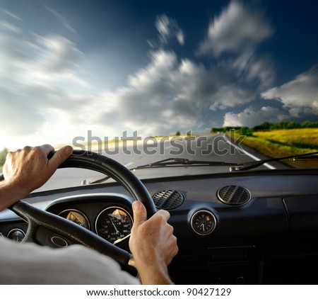 Hands of a driver on steering wheel of a car and empty asphalt road with motion blurred sky