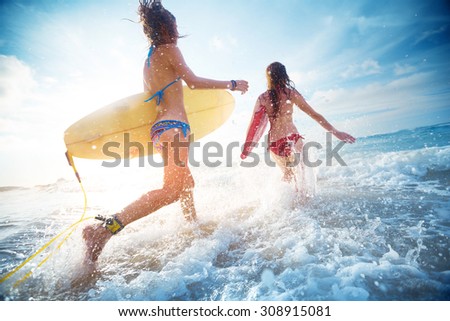 Two ladies running into the sea with surf boards