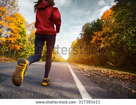 Lady running on the asphalt road through the autumn forest