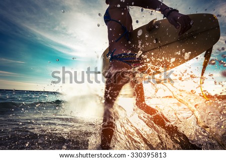 Lady with surfboard running into the sea with lots of splashes