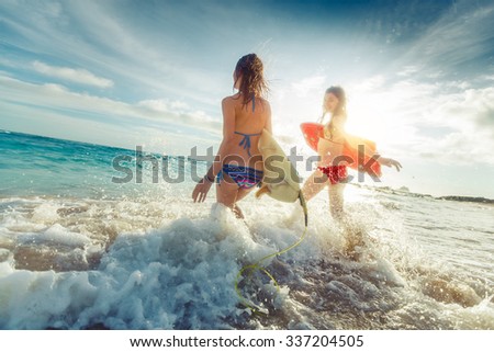 Two ladies running into the sea with surf boards