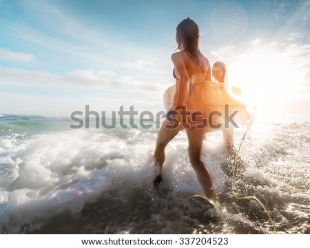 Two ladies running into the sea with surf boards at sunset