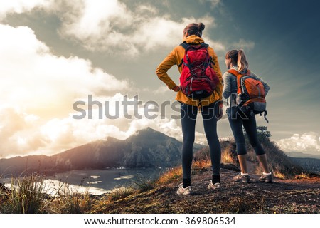 Two ladies hikers standing on top of the mountain and enjoying valley view