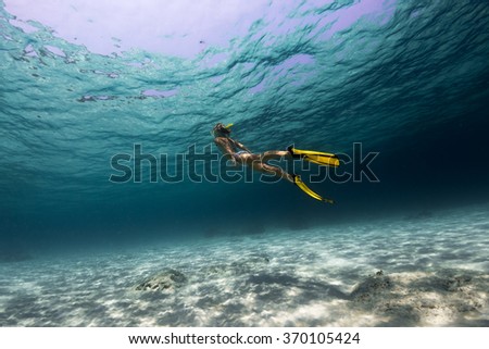 Lady swimming underwater over the sandy bottom in a tropical sea