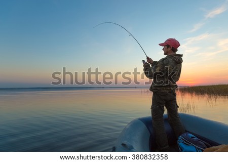 Man fishing from the boat on the lake at sunset