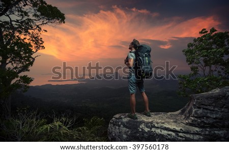 Hiker standing on top of the mountain and watching sunset over the valley