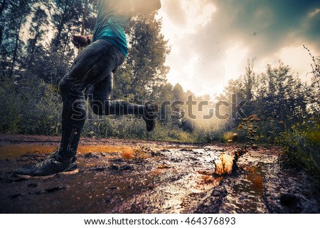 Trail running athlete crossing the dirty puddle in the forest