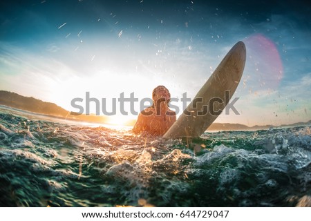 Young happy man moves through breaking waves in the ocean with his surf board and makes a lot of splashes