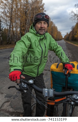 Mature bicycle tourist with his loaded bike on an asphalt autumn road