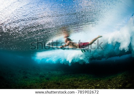 Young surfer dives under the ocean wave with surf board and performs trick named in surfing as a Duck Dive