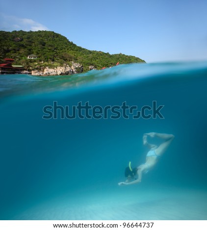 Young woman diving on a breath hold in a clear tropical sea with green island on the background