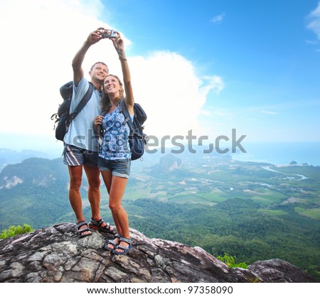 Happy couple with backpacks making a snapshot of themselves on top of a mountain