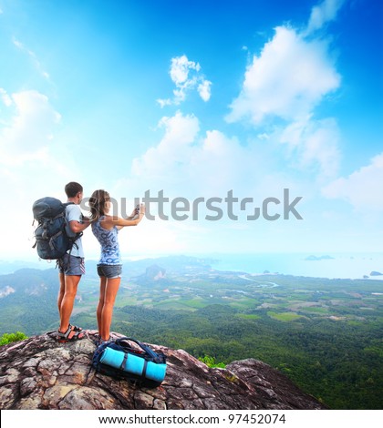 Young tourists with backpacks taking photo of a valley from top of a mountain Young tourists with backpacks taking photo of a valley from top of a mountain