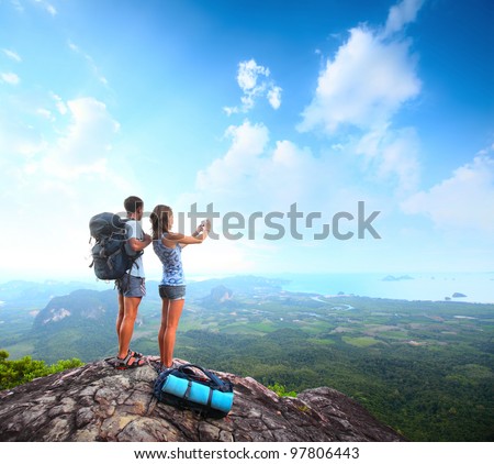 Young tourists with backpacks taking photo of a valley from top of a mountain