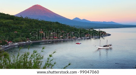 Volcano Agung (Bali island, Indonesia) lighted by rising sun and calm lagoon with sail boat