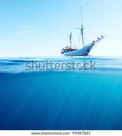 Sail boat in tropical calm sea on a surface and underwater sea view with sun beams