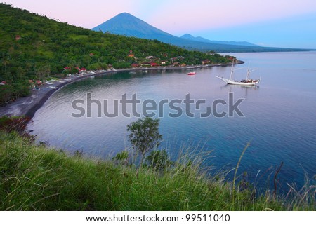 Calm lagoon with sail boat and buildings in forest on a hill side