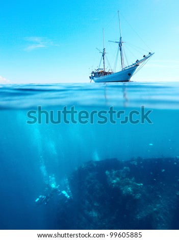 Sail boat in a tropical calm sea on a surface and divers underwater exploring a shipwreck