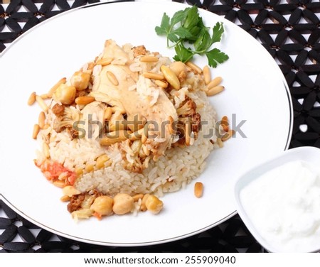 Traditional Middle Eastern chicken and cauliflower rice dish with fried nuts (Makloubeh) and yogurt on wood mat background