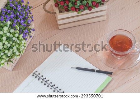 Spiral notebook with tea and flowers on wood background
