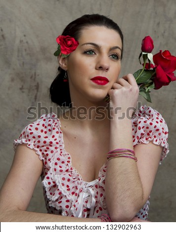 Retro lady wearing red polka dot blouse while holding red roses and wearing one in her hair.