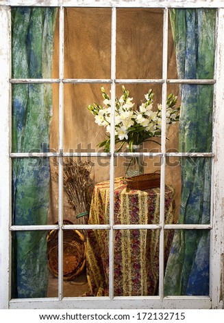 View of interior of home through rugged weathered and worn window pane with flowers on table and wicker baskets (Vintage feel to this image)