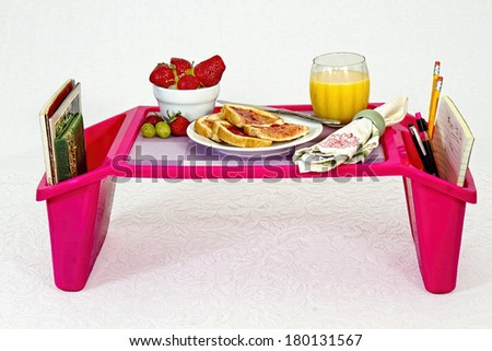 Breakfast tray with toast, strawberries, orange juice and books and things to do in side pockets.