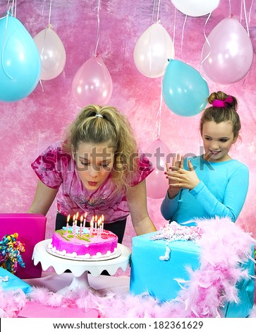 Girl\'s birthday party celebration with cake and balloons with girl in background watching friend preparing to blow out candles