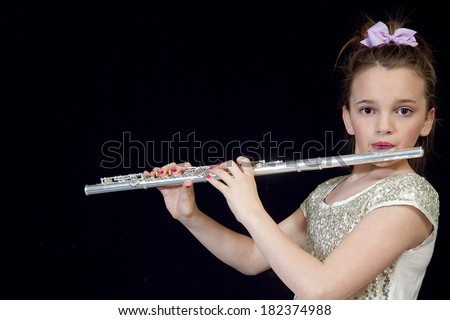 Young preteen girl playing her flute against black background
