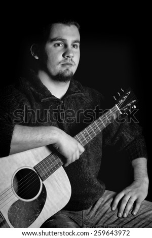 Black and white image of senior high school male holding his guitar with black background.  Rembrandt lighting.