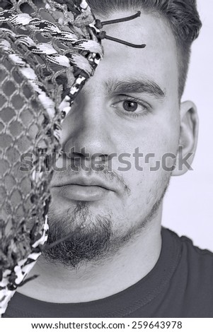 Black and white image (Closeup) of a masculine high school senior with his lacrosse stick covering half of face.