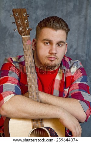 Closeup of a High School senior male posing with his guitar wearing red plaid shirt
