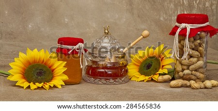 Narrow strip with sunflowers, jars of honey and jar of peanuts with extras laying next to it.  Red burlap covers on lids with ties.