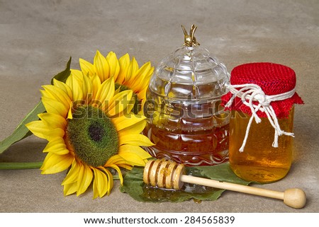 Honey in jars with wand laying next to it coated in honey.  Sunflowers next to honey jar.