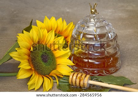 Closeup of Honey jar, sunflowers and honey wand covered in honey.