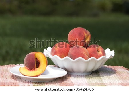 Peaches in a bowl on outside table with small plate and sliced peach on it.